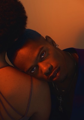 Two models in amber light, one resting his head on the other's shoulder
