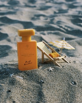 Mango Hour fragrance bottle on sand with a miniature deck chair and parasol