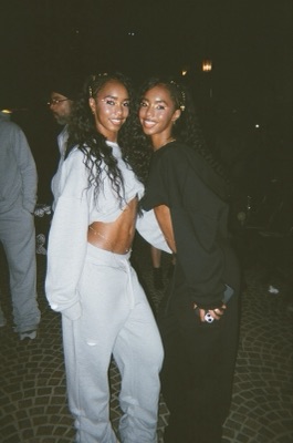Two models with gold glitter eye makeup on a cobblestone street at night